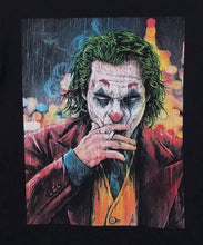 Load image into Gallery viewer, &quot;2019 Joker Smoking T-Shirt featuring a colorful graphic of the Joker in makeup and suit, smoking against a city lights backdrop. Black unisex tee, available in sizes Small to 3XL.&quot;



