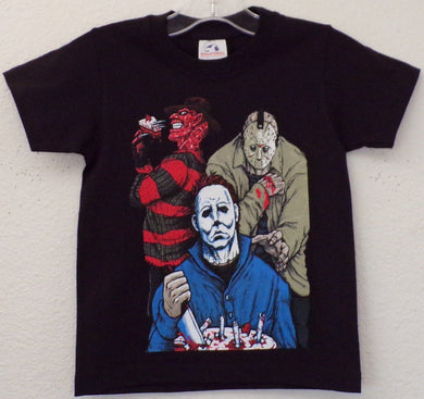 Youth T-shirt featuring a silkscreen design of Michael Myers, Freddy Krueger, and Jason Voorhees sitting around a campfire with a birthday cake. Freddy is holding a knife and a slice of cake, while Jason stands behind Michael, who is in his signature blue jumpsuit. Available in sizes XS-XL.